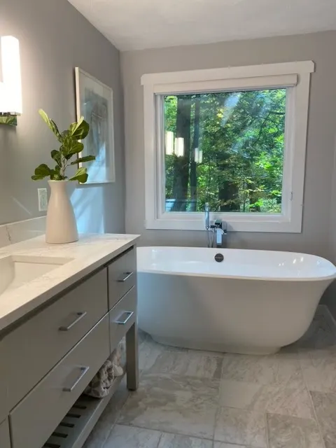 Finished bathroom with a freestanding tub under a window, a floor-mounted tub filler and a double vanity