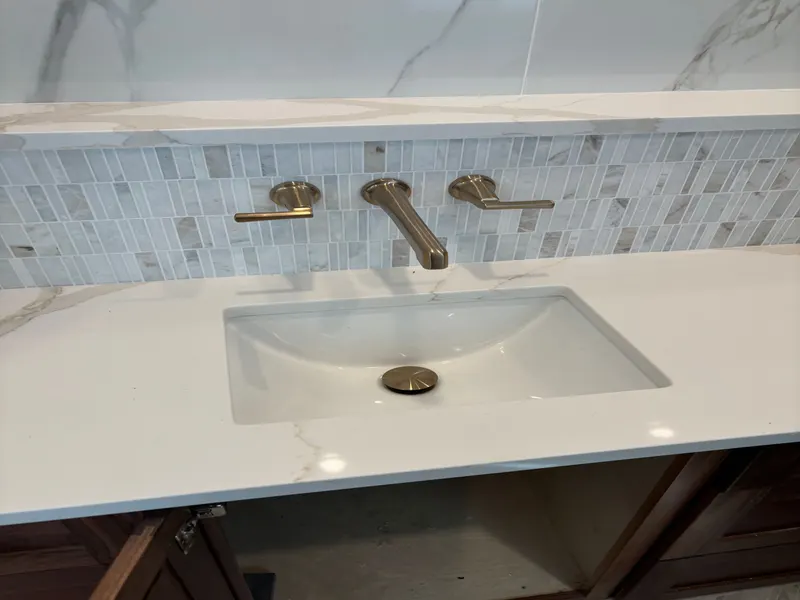 Finished vanity with an undermount sink and a brushed-brass wall-mount faucet set into a marble mosaic tile strip