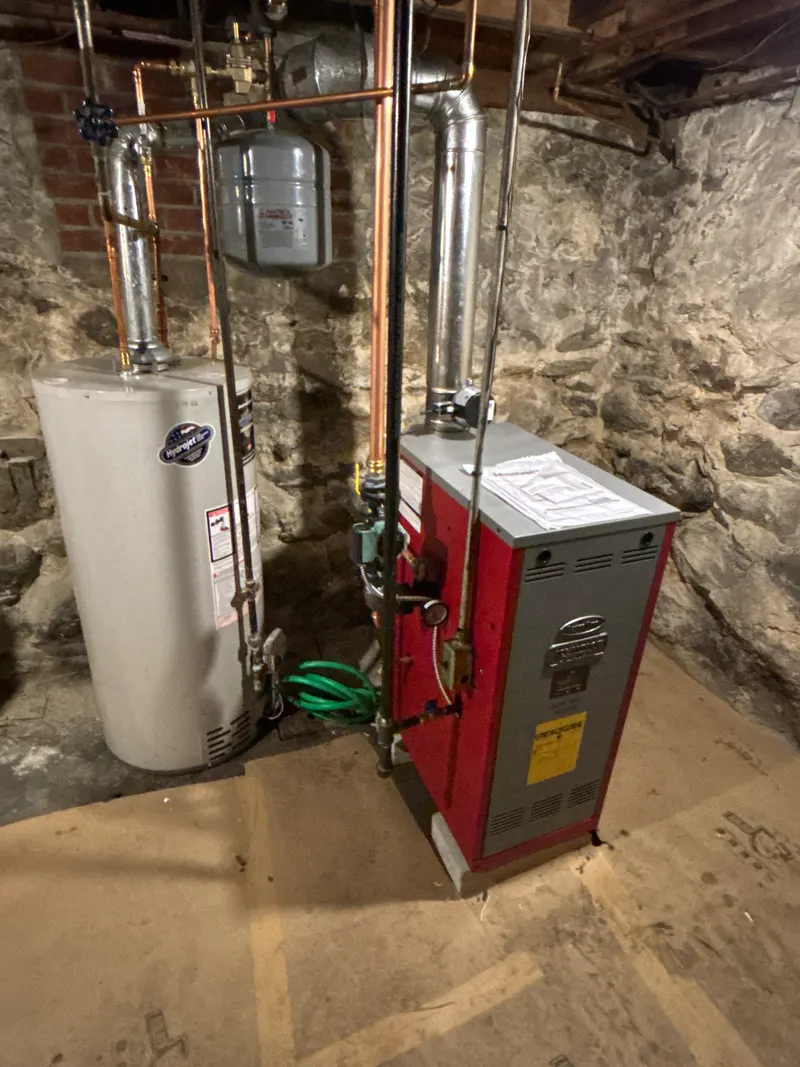 Red boiler and a tank water heater in a fieldstone basement, with new copper piping, venting and an expansion tank overhead