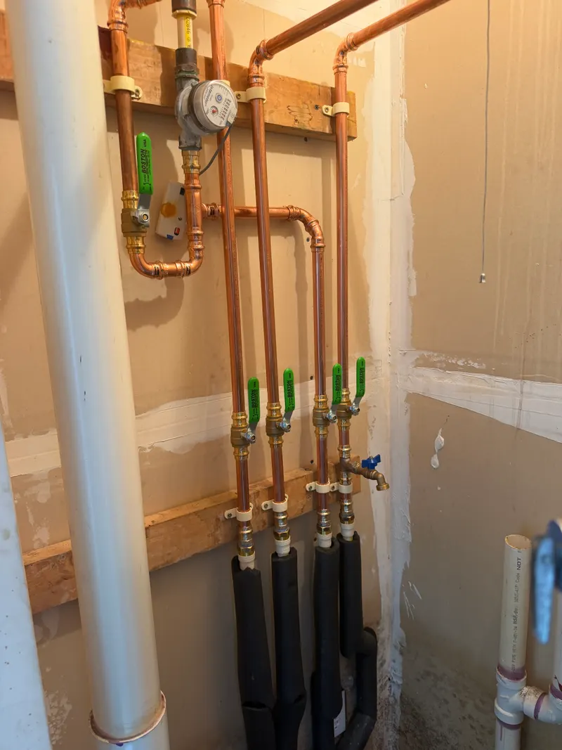 New copper water piping beside the water meter, split into separate lines with green-handled shutoff valves
