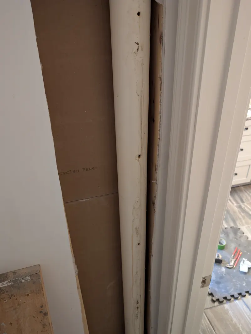 Old painted drain stack running up inside an opened wall, before replacement
