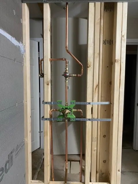 Copper supply lines and a shower valve roughed in between open wall studs, strapped and ready for inspection