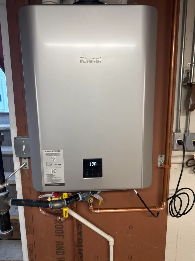 Rinnai tankless water heater mounted on a backboard, with new copper water lines and connections piped in below it