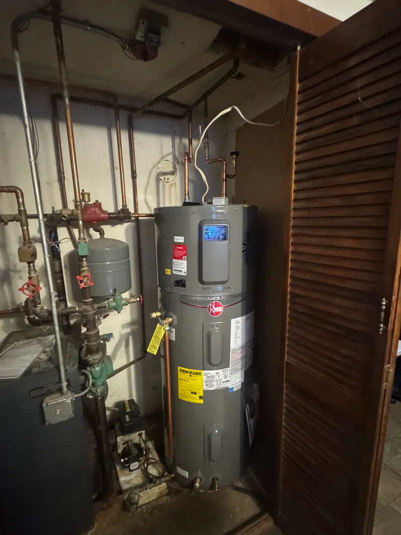 New Rheem electric water heater installed in a utility closet beside the boiler and its expansion tank